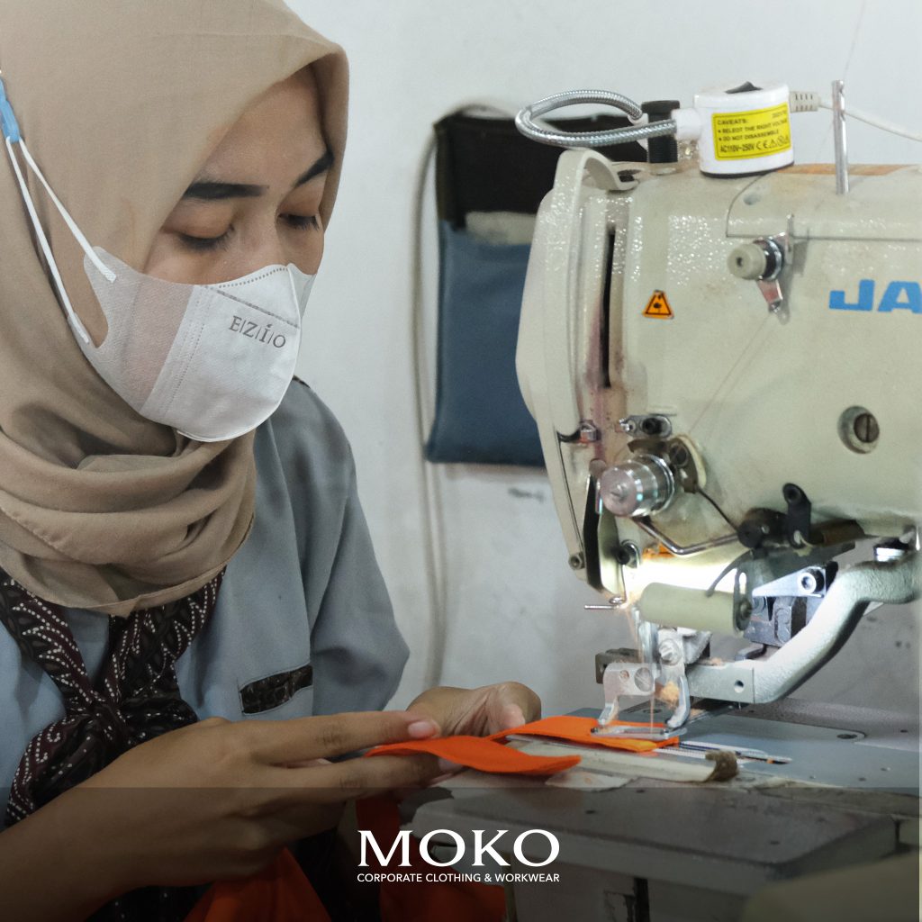 Penjahit wanita berhijab sedang menjahit seragam menggunakan mesin jahit di workshop jasa pembuatan baju seragam profesional Indonesia